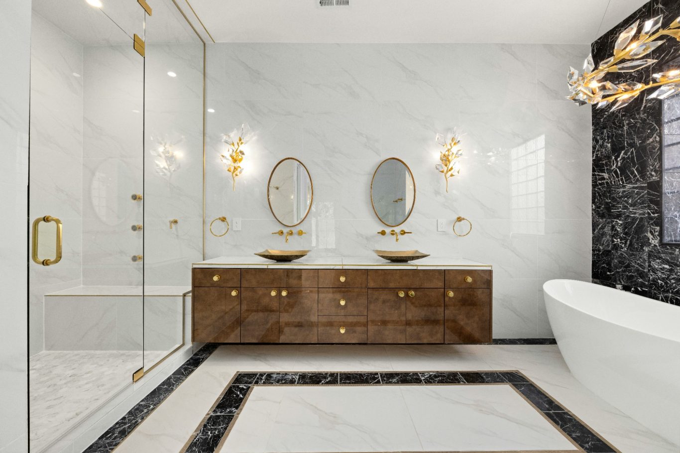 Modern bathroom remodel with marble floors, counter top, and walls. Also brown cabinets, gold accents, and a white bathtub in Marco Island.
