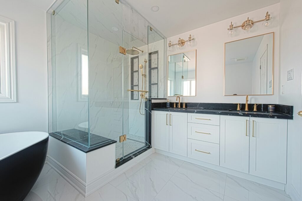 Modern bathroom remodel in North Naples with white cabinets, black marble counter top, and gold accents.