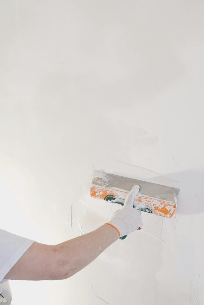 A gloved hand applying plaster to a wall with a trowel in Naples.