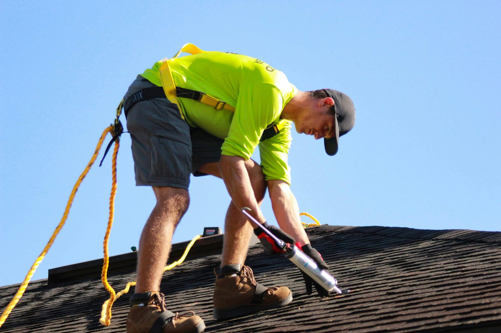 A handyman works on a roof, using a caulking to do roof repairs.