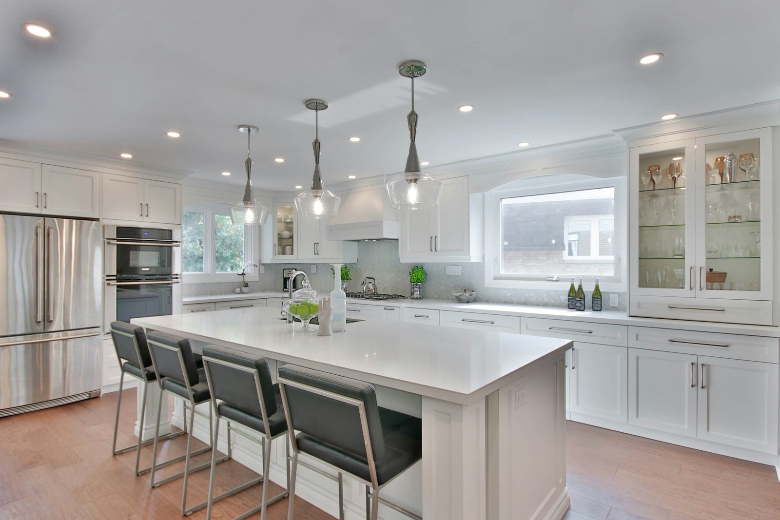 A modern kitchen with white cabinets and countertops, grey chairs, and modern lights remodeled in Marco Island.