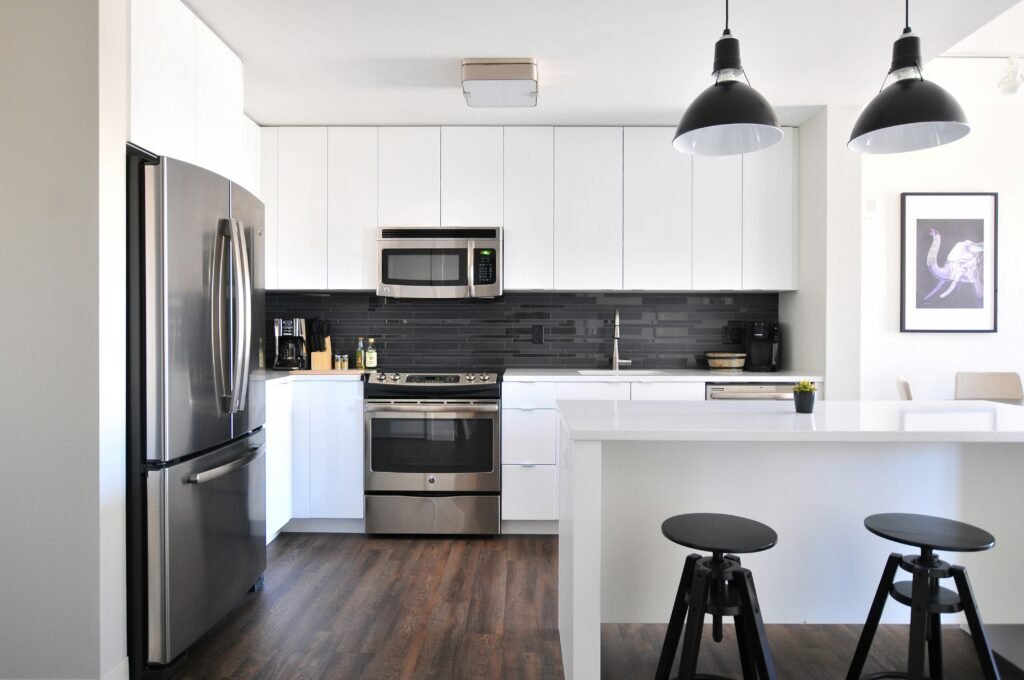 Modern Kitchen Remodel in Old Naples with LVP flooring, white cabinets and counter tops, and sliver appliances.