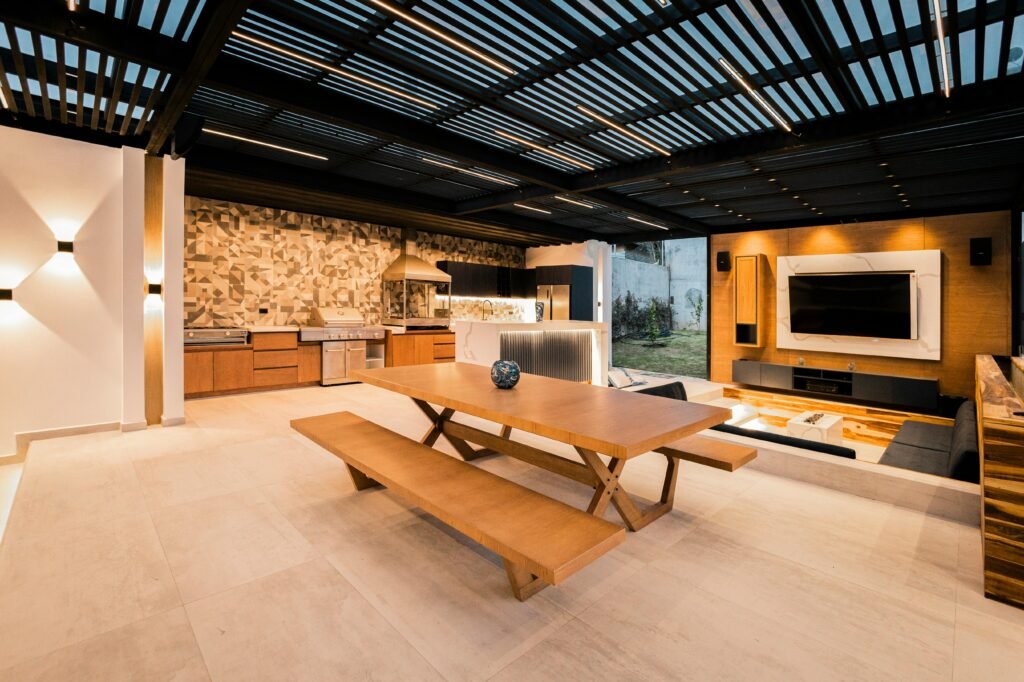 Modern open-concept outdoor living space remodel featuring kitchen, dining area, and lounge with wooden elements.