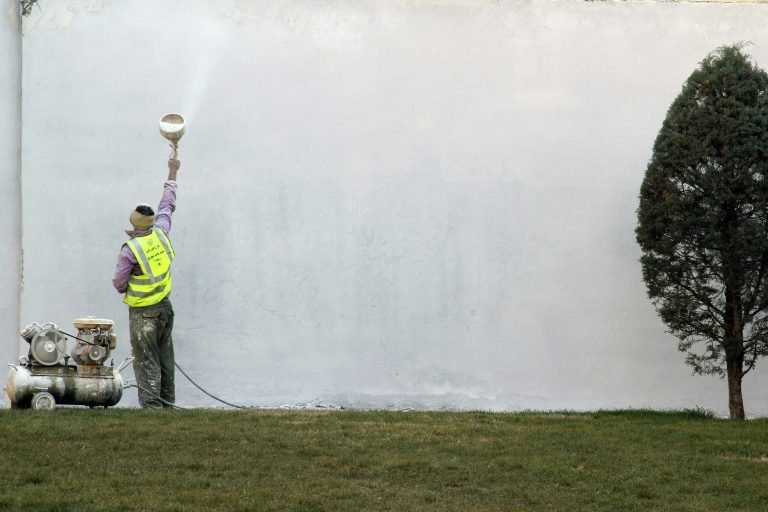 A Handyman using a paint sprayer to paint the outside of a home in North Naples.
