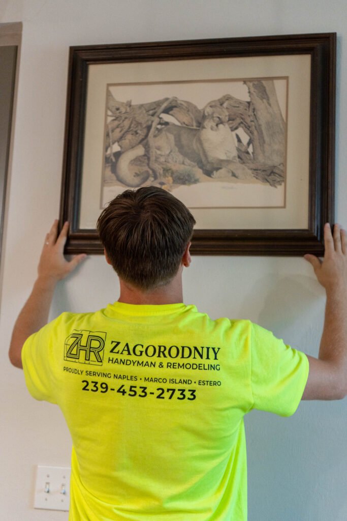 A handyman handing a photo of a grey and white lion in a brown frame on a white wall in Naples.