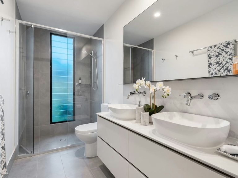 Modern bathroom with double sinks, glass shower, and light gray tile accents in Naples, FL.