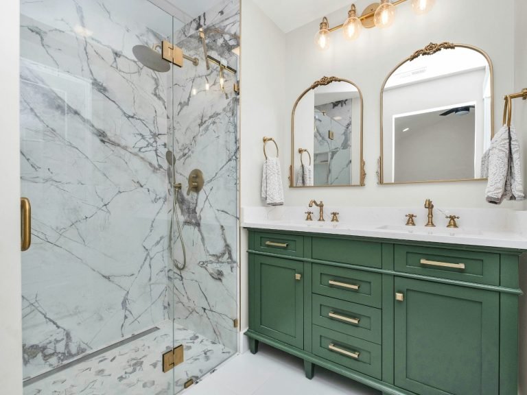 Luxurious bathroom with marble shower, green vanity, and gold fixtures in North Naples.