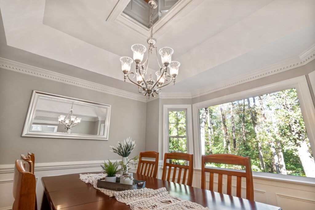 Custom, white crown moulding in a dining room with grey walls and a chandelier in Naples.