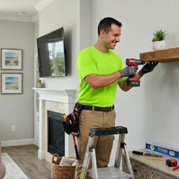 A handyman in a neon green shirt using a drill to install a shelf in a living room in Old Naples.