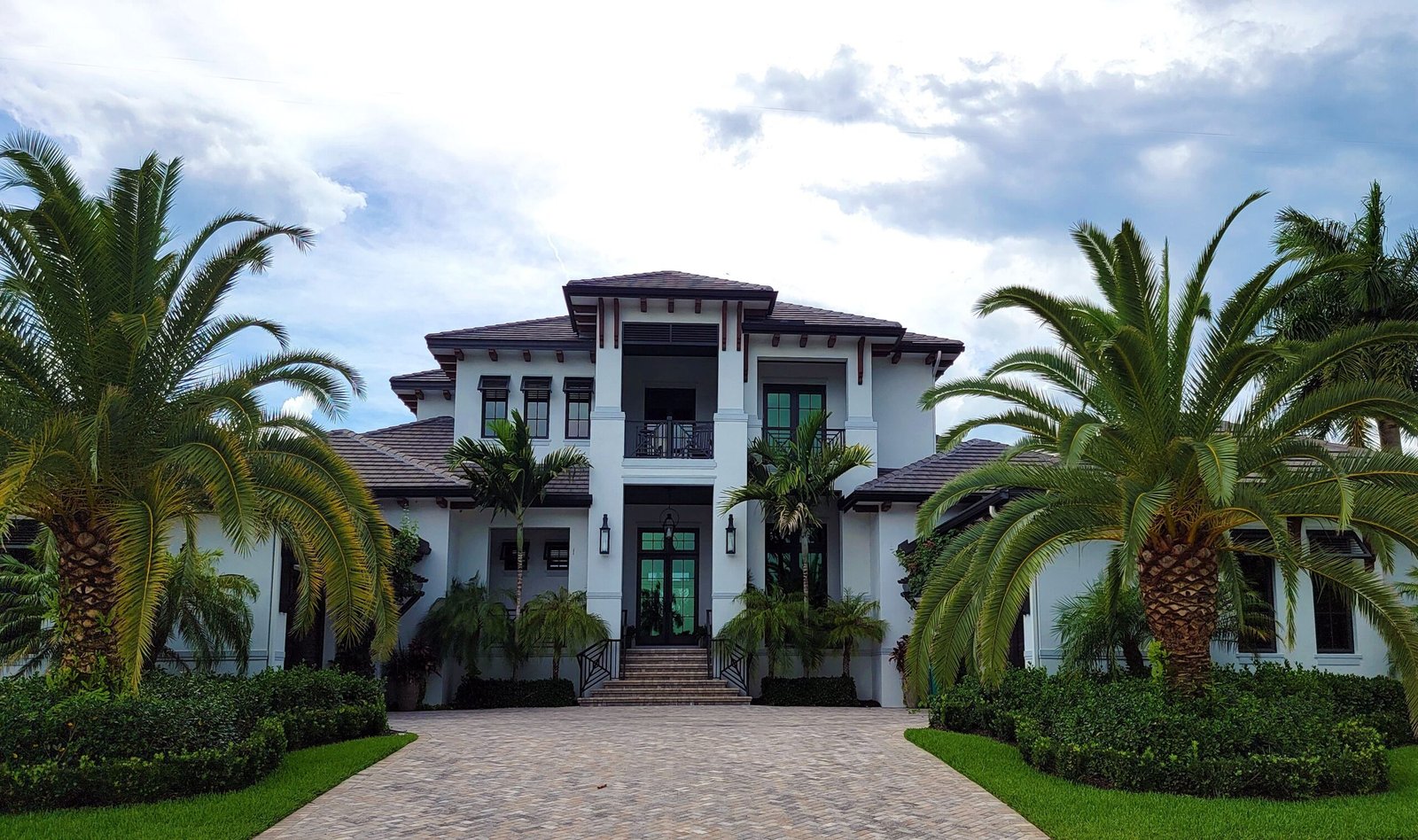 Modern, white home with palm trees in the font and a paver driveway in Naples.