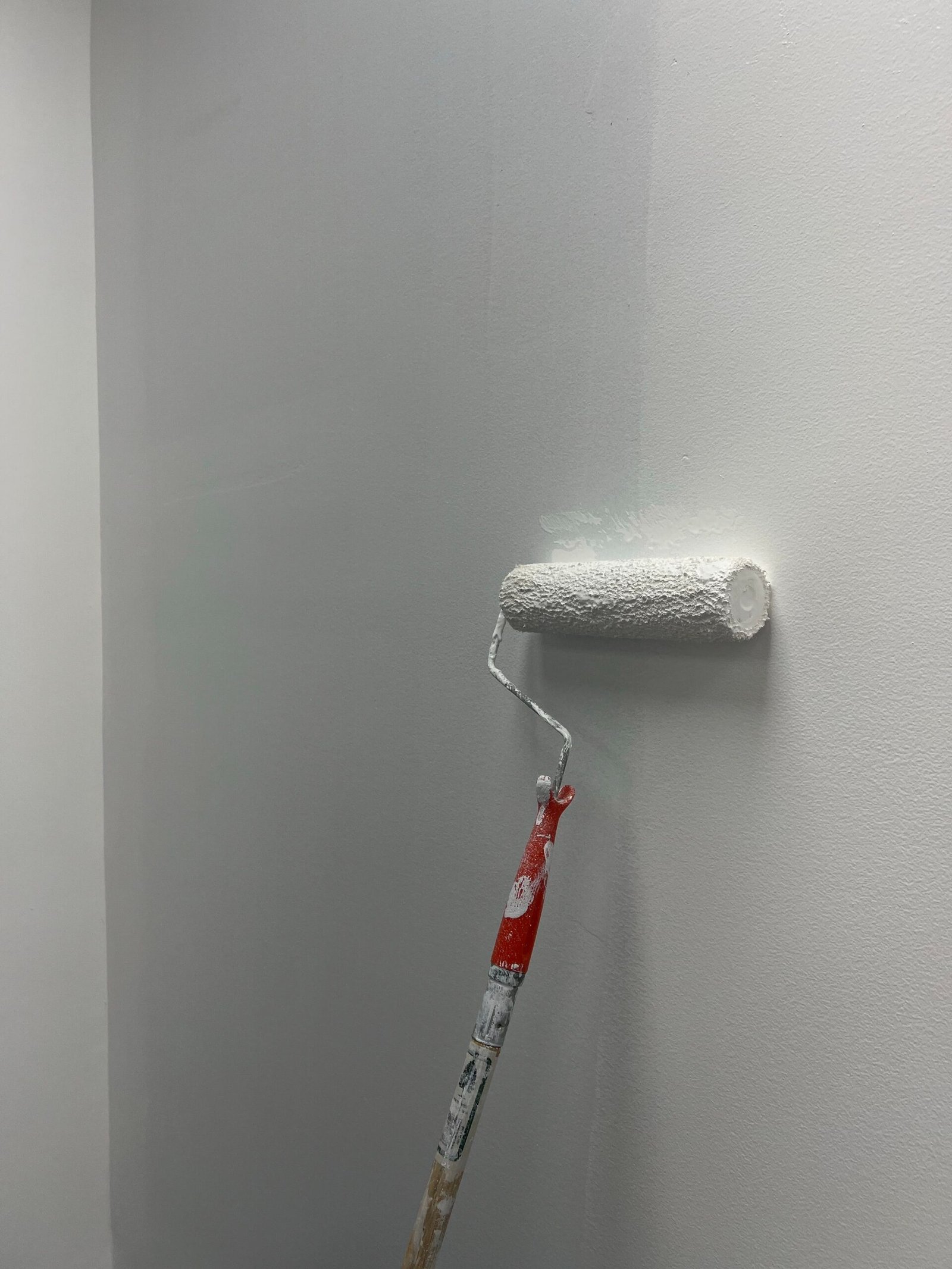 A long roller brush painting a grey wall white in North Naples.