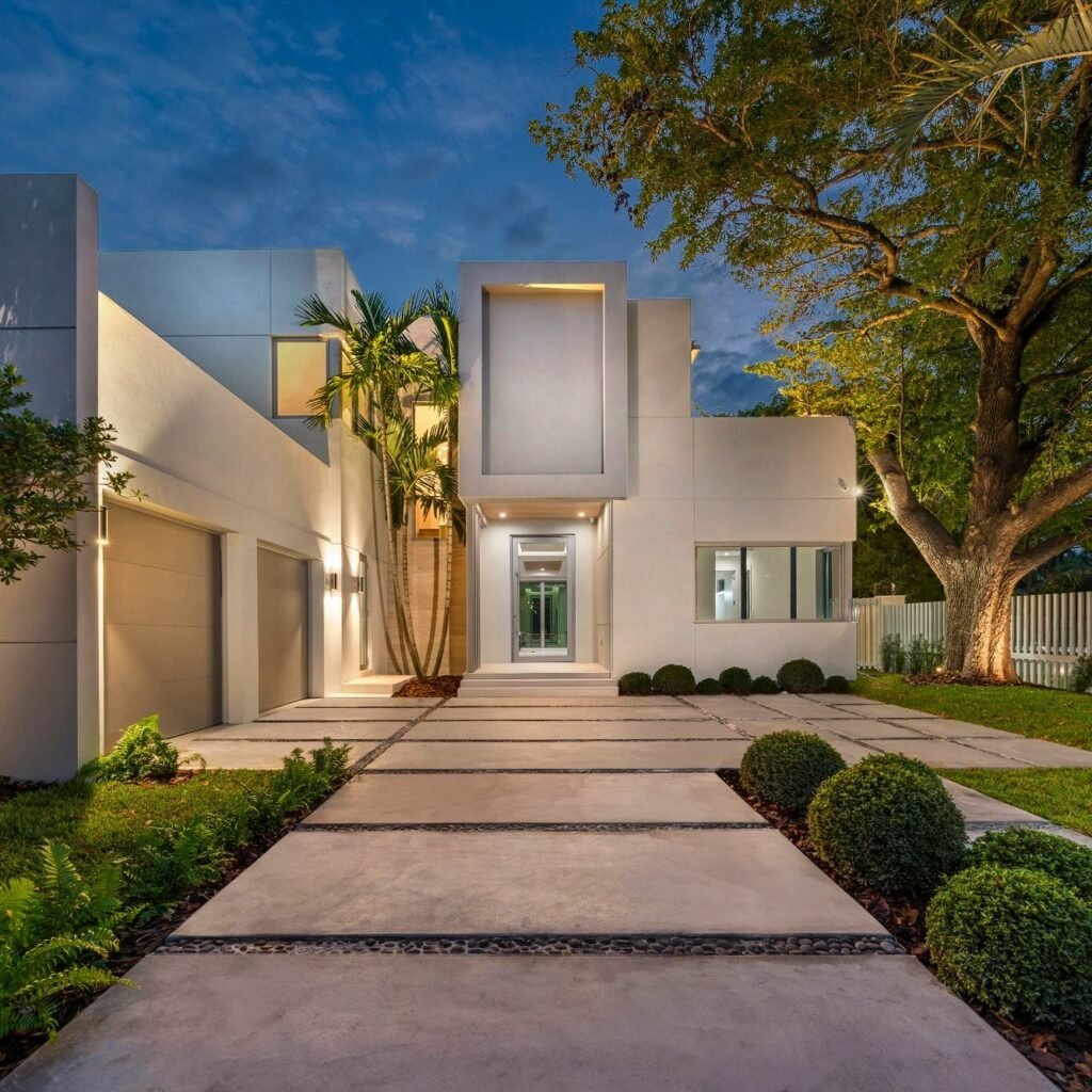 Modern house with a light exterior paint, custom tile pathway, and tropical plants at dusk in Naples, FL.