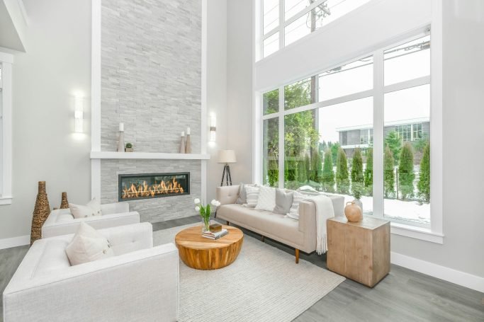 Modern living room with a stone fireplace, white furniture, and large windows in Old Naples.