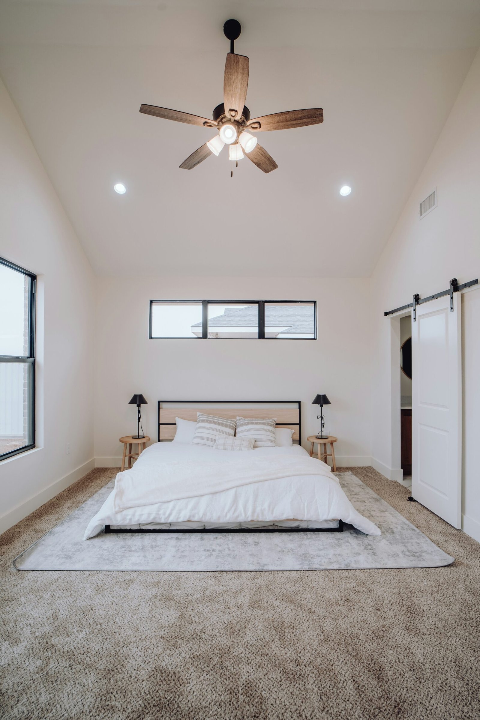 A bedroom with cream colored walls, wood ceiling fan, and tan carpets in Marco Island.