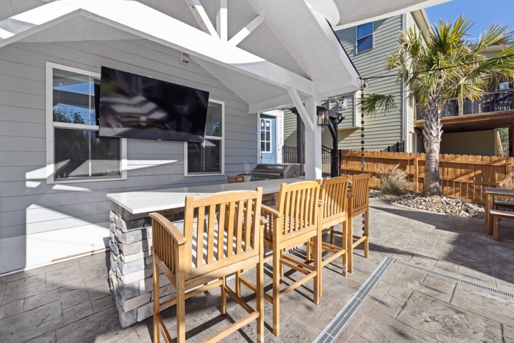 Outdoor patio with a table, bar stools, and a mounted TV on a light gray house in Naples.