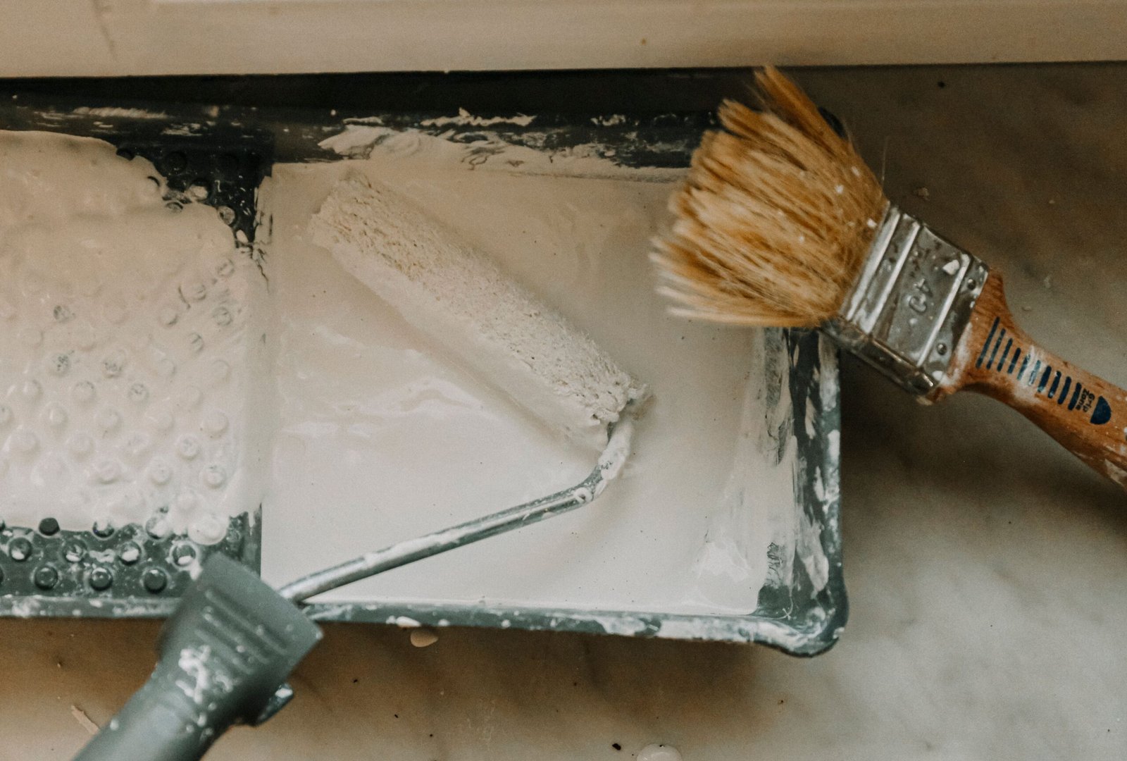 A Paint try with white paint, a regular brush, and a roller brush in Marco Island.
