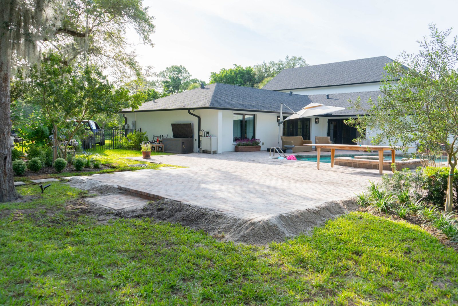 A paver patio addition to a white home that has a pool near it in North Naples.
