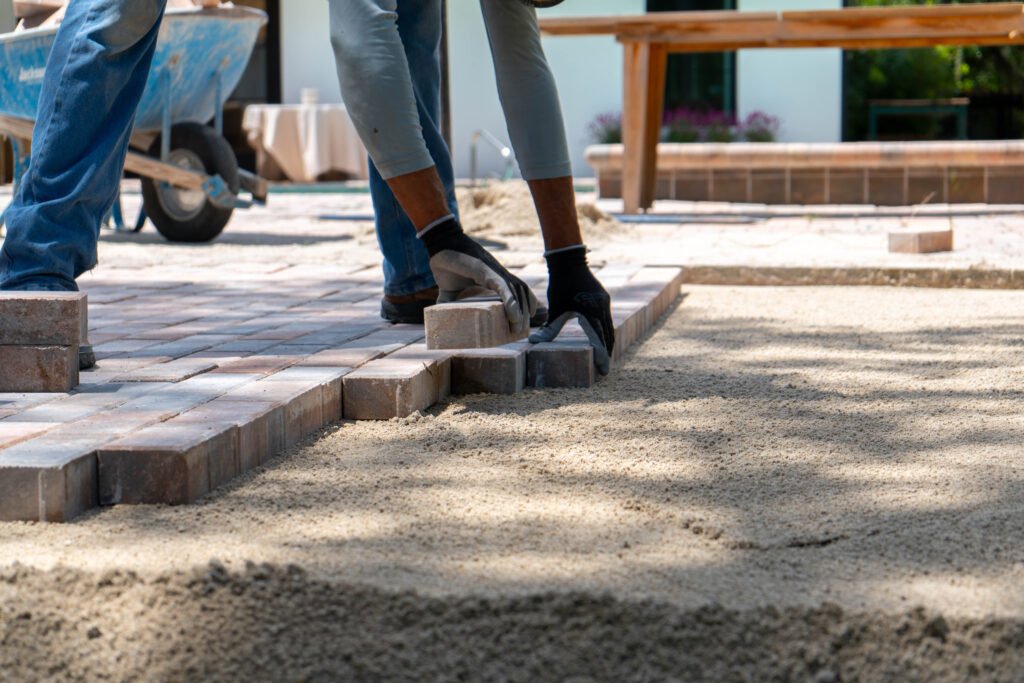 A worker using black gloves to place pavers onto a flat, sand pad in North Naples.