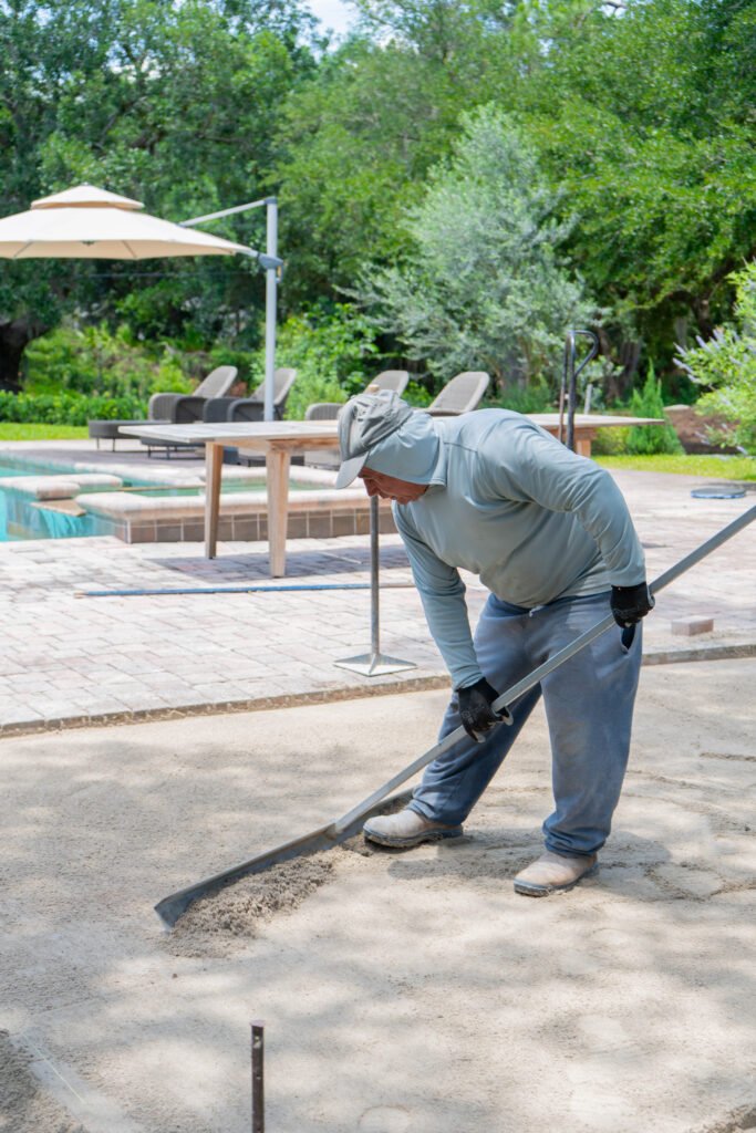 A worker leveling sand to install a paver patio in North Naples.