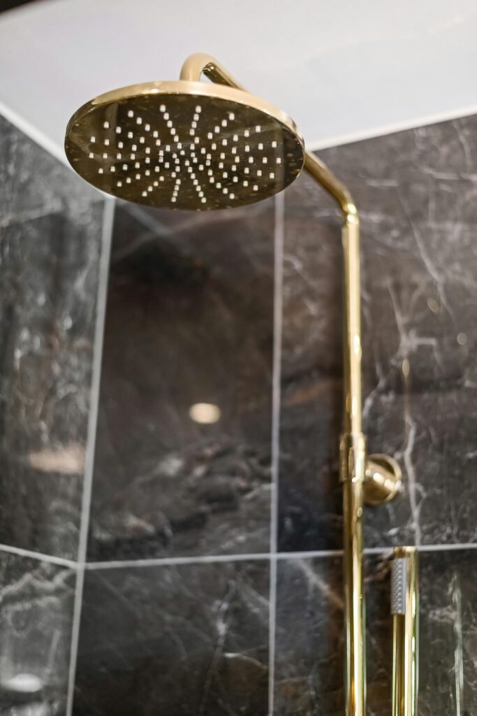 Gold showerhead mounted on a sleek modern wall with dark marble tiles.