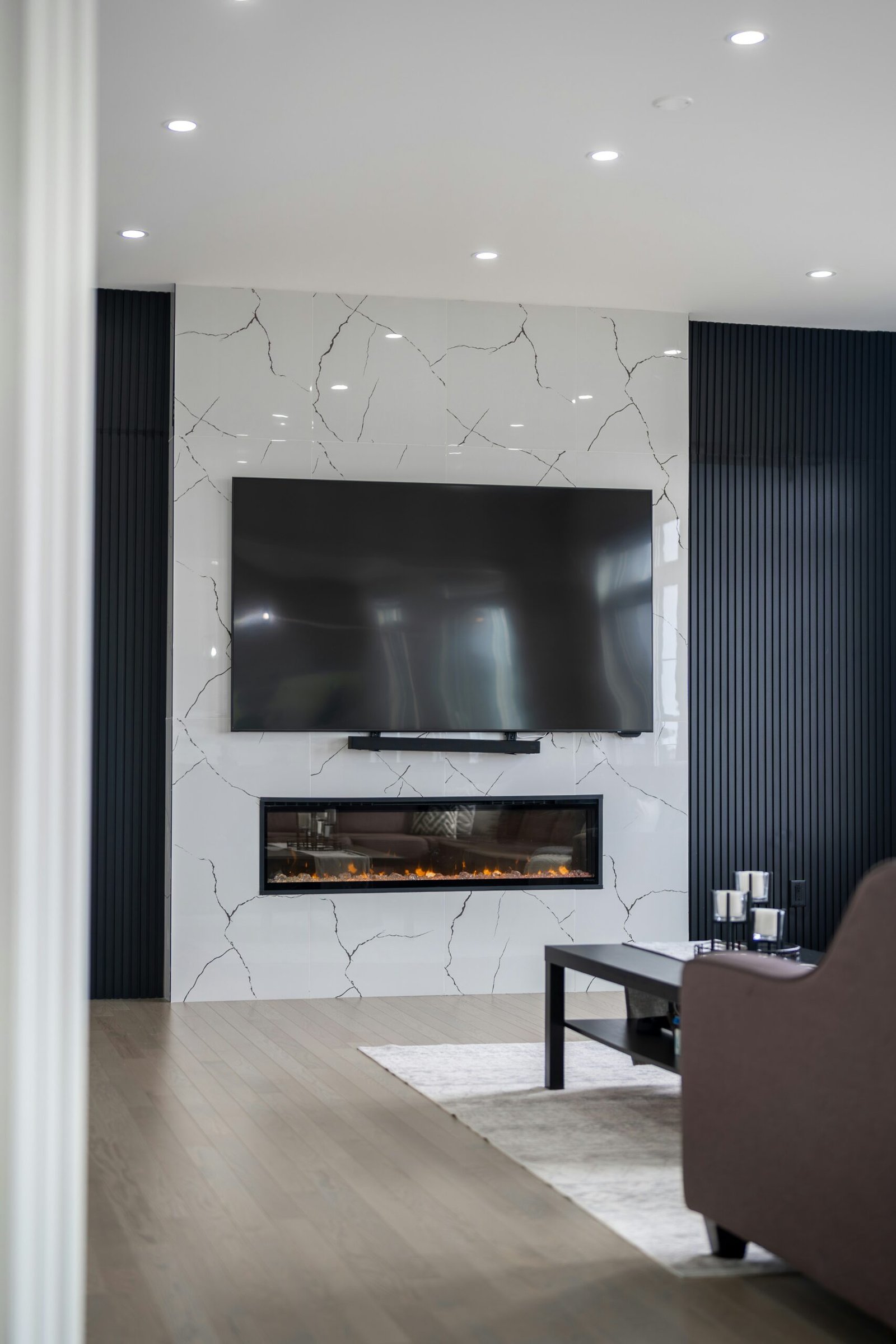 Modern living room with a large TV mounted on a tile accent wall, wood floors, and a fire place in Estero.