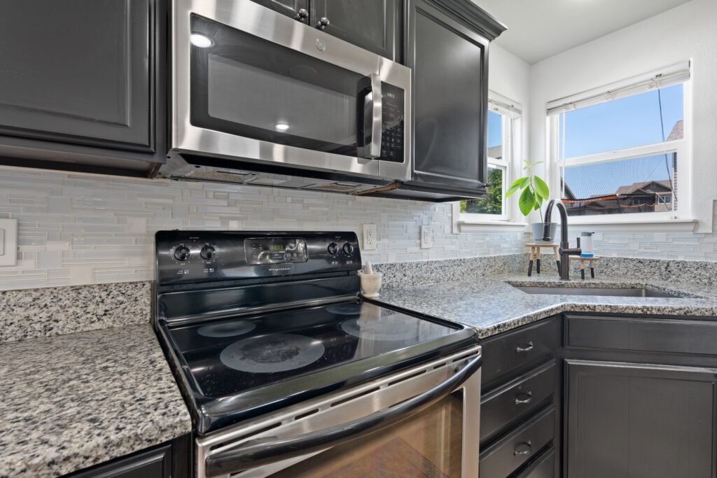 Modern kitchen with granite countertops, stainless steel appliances, and a shiny, light grey backsplash in Naples.