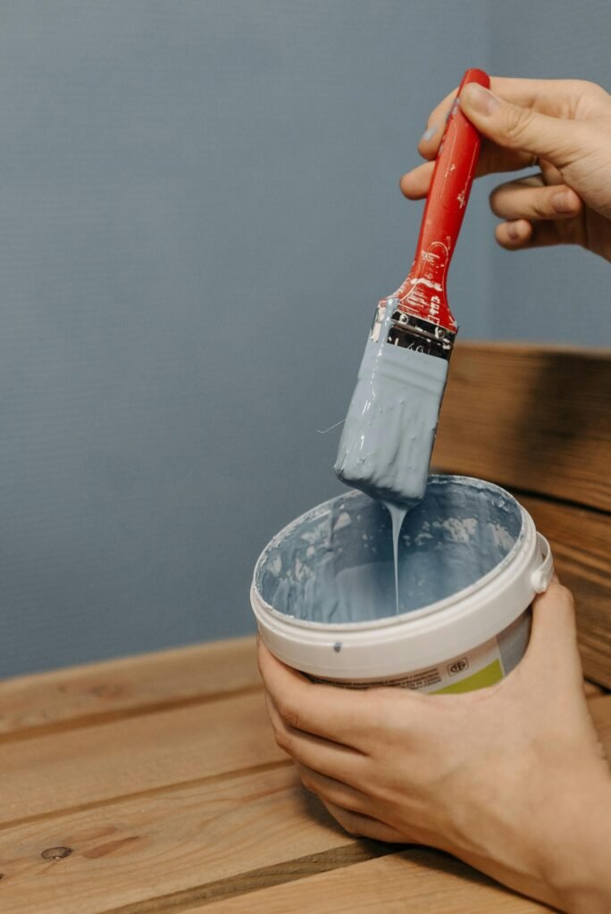 Paint touch up in Naples FL. A Grey wall with someone hold a bucket of grey paint and a paint brush.