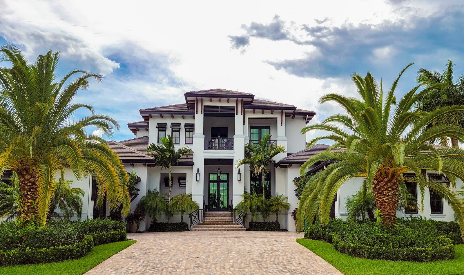 Modern, white home with palm trees in the font and a paver driveway in Naples.
